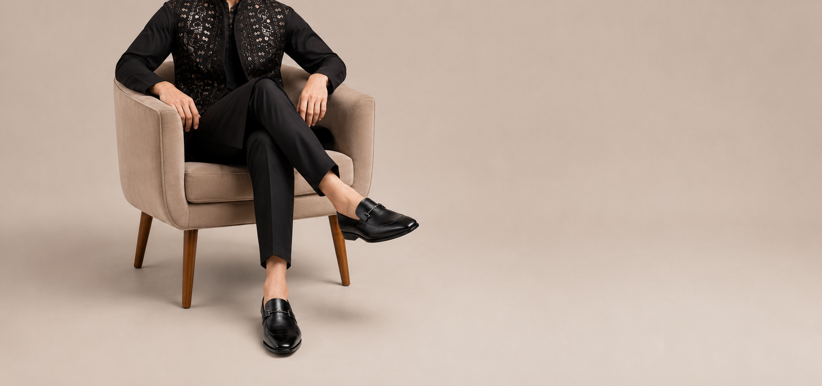 Person seated in beige armchair wearing black leather bit loafers with black tailored outfit
